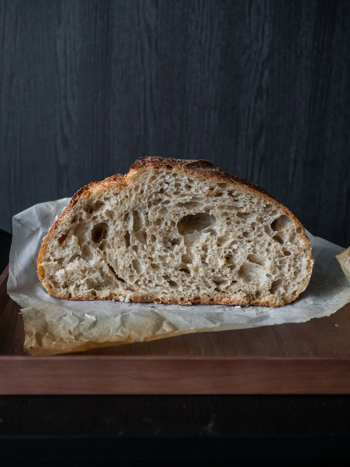 A sourdough loaf cut in half on baking paper, on a dark wooden board.