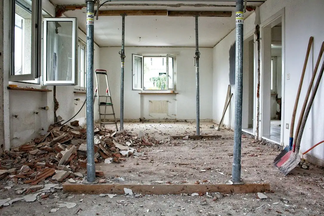 A room stripped back to the walls, with steel props holding up the ceiling, broken plaster on the floor and shovels by the wall.